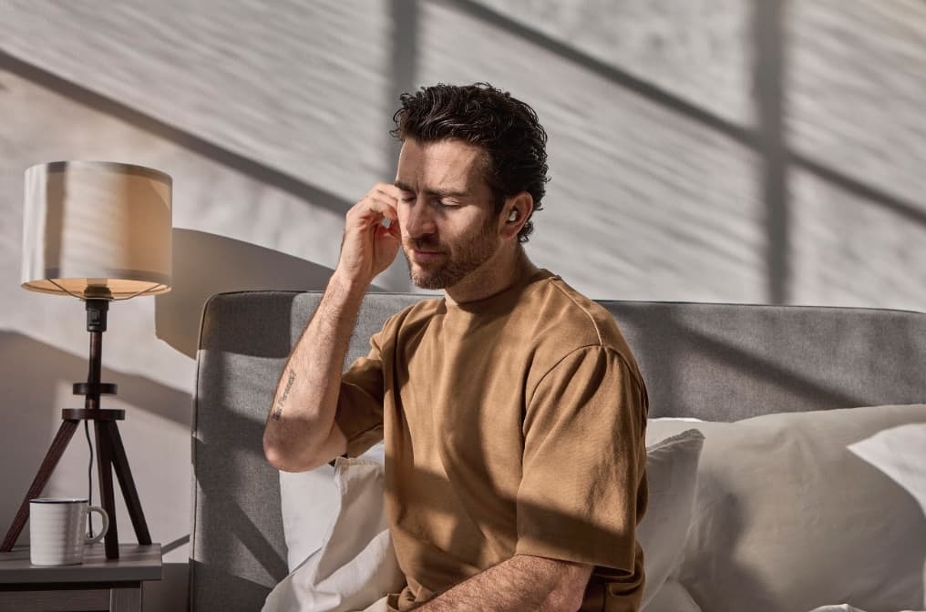 A man sitting in bed with his hand beside an earbud.
